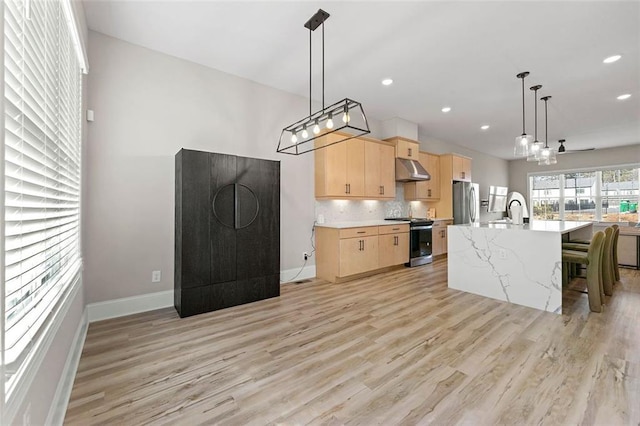 kitchen with light brown cabinetry, decorative light fixtures, an island with sink, stainless steel appliances, and decorative backsplash