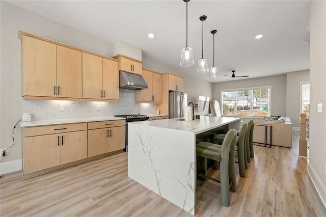 kitchen with stainless steel appliances, a kitchen island with sink, light brown cabinetry, and a breakfast bar