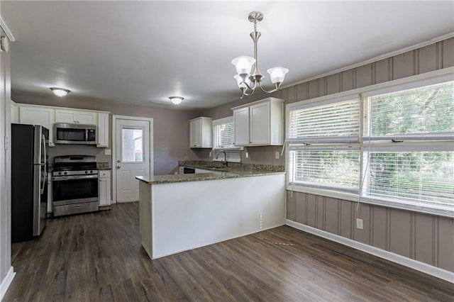 kitchen with pendant lighting, dark stone counters, dark wood-type flooring, appliances with stainless steel finishes, and white cabinetry