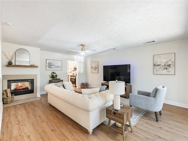 2466 Thrasher Rd, Buford, GA 30519 - living room featuring light wood finished floors, a multi sided fireplace, baseboards, a textured ceiling, and ceiling fan