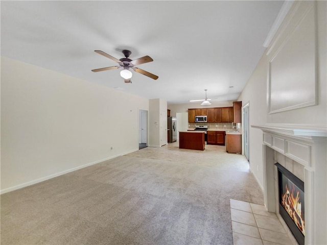 unfurnished living room featuring light colored carpet, a tiled fireplace, and ceiling fan