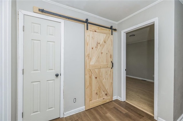 interior space featuring a barn door, a closet, wood-type flooring, and ornamental molding