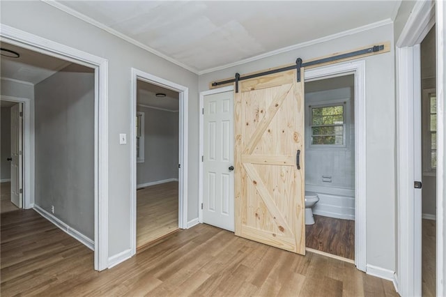 unfurnished bedroom featuring a barn door, crown molding, ensuite bath, and wood-type flooring