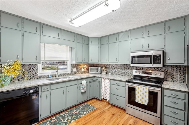 kitchen featuring light wood-style flooring, tasteful backsplash, appliances with stainless steel finishes, and a sink