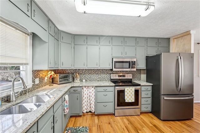 kitchen featuring a sink, gray cabinetry, stainless steel appliances, light wood-style floors, and backsplash