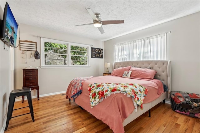 bedroom featuring a ceiling fan, baseboards, wood-type flooring, and a textured ceiling