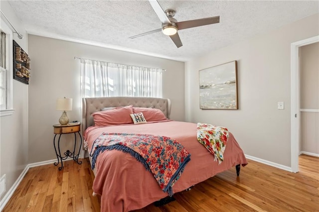 bedroom with baseboards, a textured ceiling, light wood-style flooring, and a ceiling fan