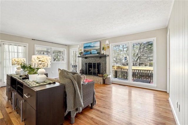 living room with a tiled fireplace, light wood-style flooring, a wealth of natural light, and a textured ceiling