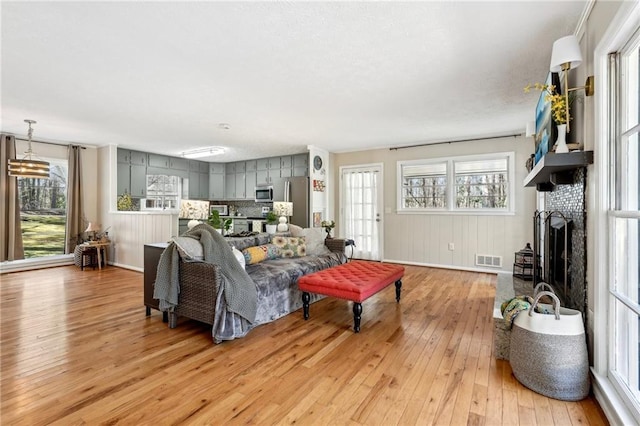 living area with a wealth of natural light, visible vents, a brick fireplace, and light wood finished floors