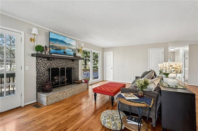 living area featuring visible vents, ornamental molding, a tiled fireplace, wood-type flooring, and baseboards