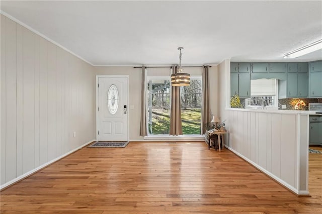 foyer with an inviting chandelier, baseboards, light wood-type flooring, and ornamental molding