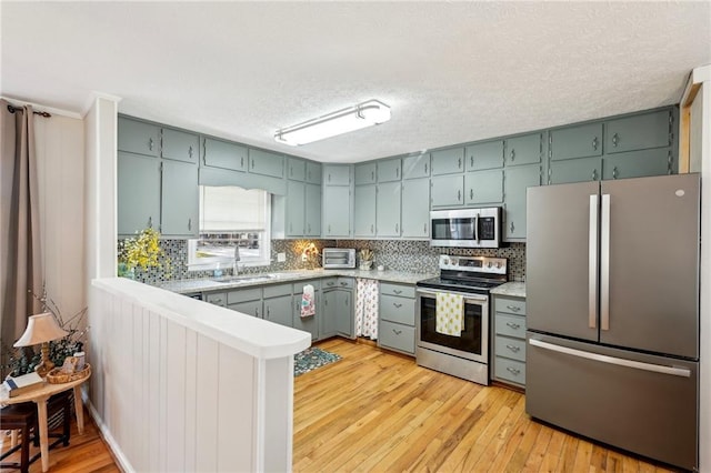 kitchen featuring a sink, appliances with stainless steel finishes, a peninsula, light wood finished floors, and light countertops