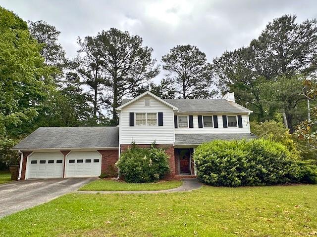 traditional home featuring driveway, a chimney, brick siding, a front lawn, and an attached garage
