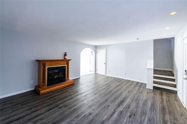 5479 Dorsett Shoals Rd, Douglasville, GA 30135 - unfurnished living room with arched walkways, dark wood-type flooring, a fireplace with raised hearth, baseboards, and recessed lighting