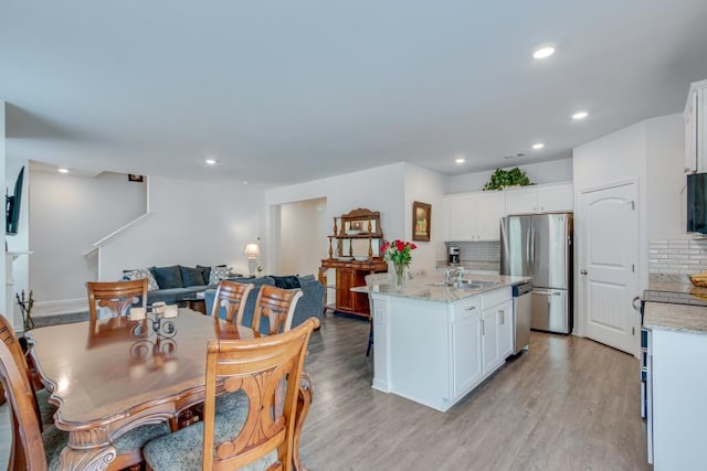 kitchen featuring white cabinetry, stainless steel appliances, light stone countertops, decorative backsplash, and a center island with sink