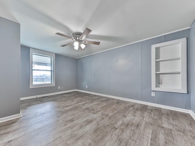 empty room featuring built in shelves, ceiling fan, and wood-type flooring