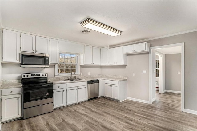 kitchen with stainless steel appliances, light countertops, white cabinets, a sink, and light wood-type flooring