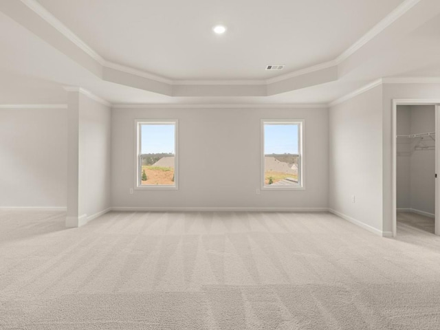 unfurnished bedroom with light carpet, a tray ceiling, a walk in closet, and visible vents