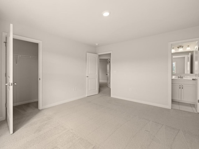 unfurnished bedroom with ensuite bathroom, baseboards, light carpet, a sink, and a walk in closet