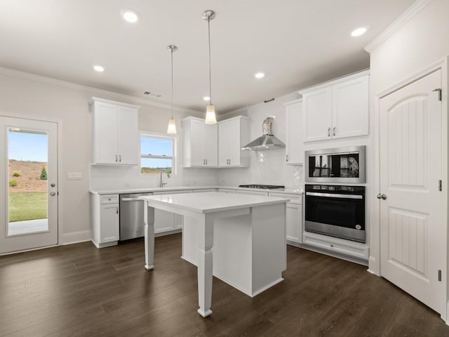 kitchen featuring wall chimney range hood, light countertops, stainless steel appliances, and ornamental molding