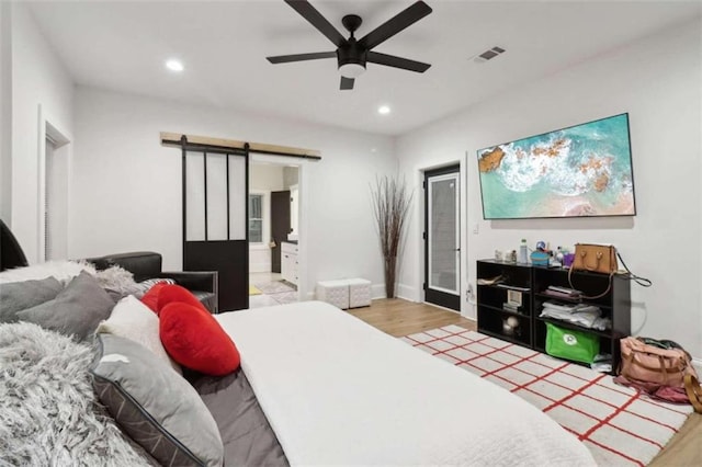 bedroom with a barn door, ensuite bathroom, ceiling fan, and wood-type flooring