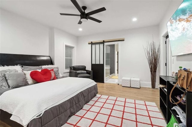 bedroom featuring a barn door, ceiling fan, ensuite bathroom, and hardwood / wood-style flooring