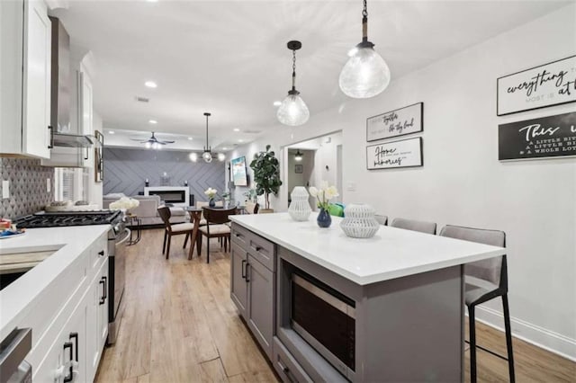 kitchen featuring a breakfast bar, white cabinets, appliances with stainless steel finishes, decorative light fixtures, and light hardwood / wood-style floors