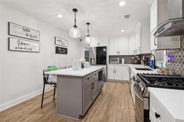 kitchen featuring stainless steel appliances, a kitchen island, decorative light fixtures, white cabinetry, and range hood