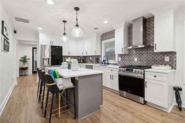 kitchen featuring sink, stainless steel appliances, white cabinetry, and wall chimney range hood