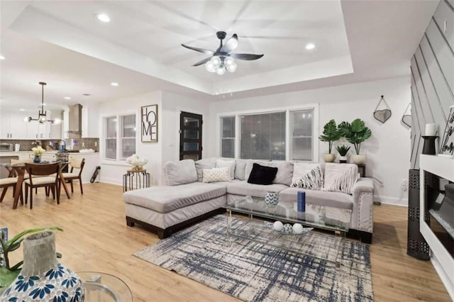 living room with ceiling fan with notable chandelier, light hardwood / wood-style floors, and a raised ceiling