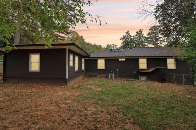 back house at dusk with a lawn and central air condition unit