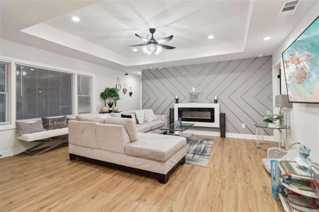 living room with wood walls, ceiling fan, light hardwood / wood-style floors, and a raised ceiling