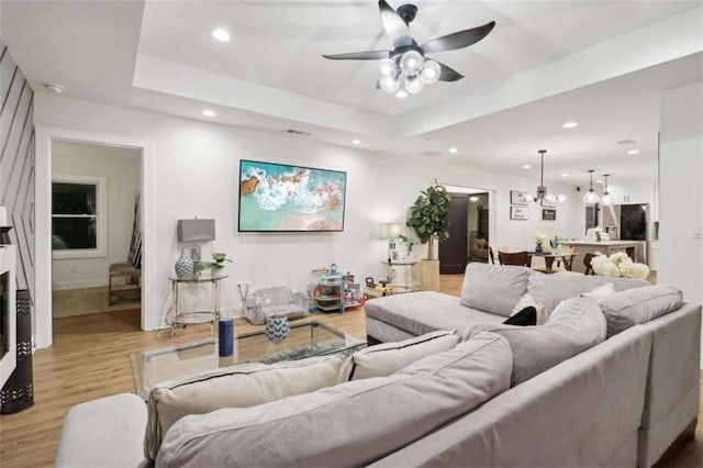 living room featuring a tray ceiling, ceiling fan, and light wood-type flooring