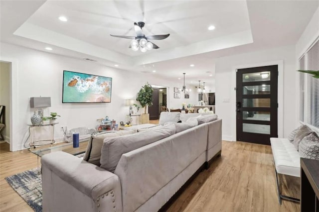 living room with light hardwood / wood-style floors, ceiling fan, and a tray ceiling