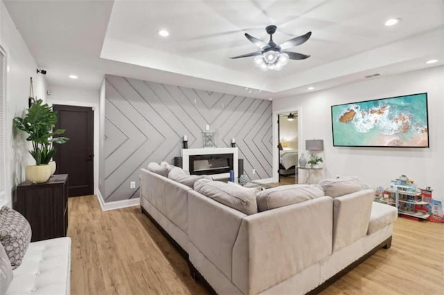 living room with ceiling fan, light hardwood / wood-style floors, wooden walls, and a tray ceiling