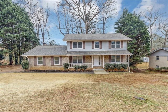 traditional-style home featuring brick siding, a chimney, covered porch, and a front yard