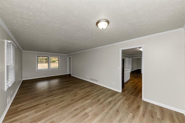 empty room with crown molding, wood finished floors, visible vents, and baseboards