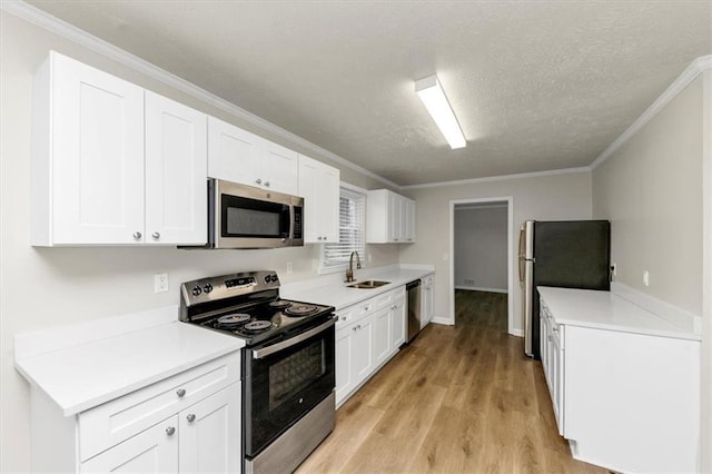 kitchen featuring appliances with stainless steel finishes, light wood-style floors, ornamental molding, white cabinetry, and a sink