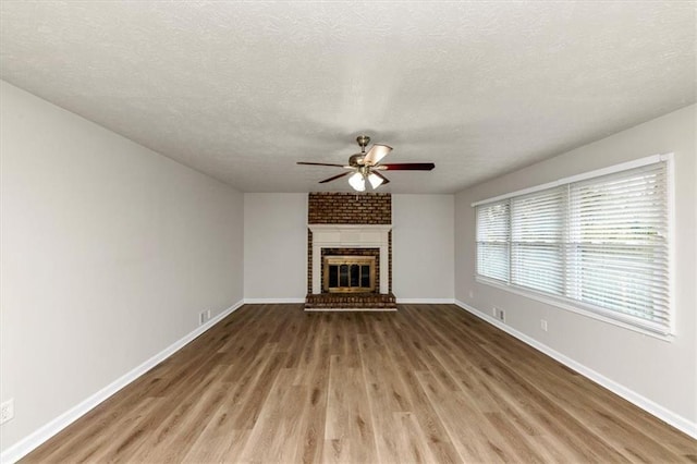 unfurnished living room featuring baseboards, a ceiling fan, wood finished floors, a textured ceiling, and a brick fireplace