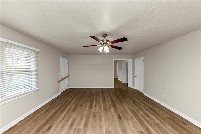 interior space with a ceiling fan, a textured ceiling, baseboards, and wood finished floors