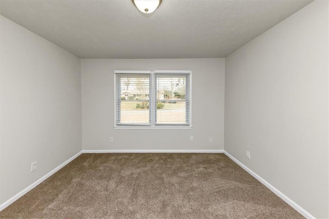 empty room with a textured ceiling, dark colored carpet, and baseboards