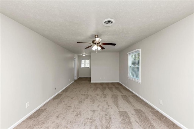 empty room featuring visible vents, light carpet, ceiling fan, a textured ceiling, and baseboards