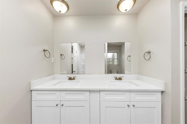 bathroom with toilet, double vanity, and a sink