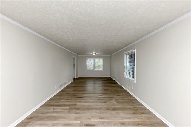 empty room with a textured ceiling, wood finished floors, visible vents, and crown molding