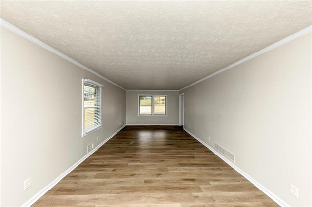 empty room with a textured ceiling, wood finished floors, visible vents, and crown molding