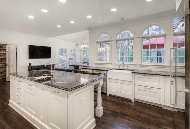 kitchen with decorative light fixtures, a kitchen island with sink, sink, and dark stone countertops