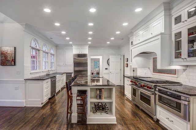 kitchen featuring white cabinetry, premium appliances, an island with sink, and dark stone counters