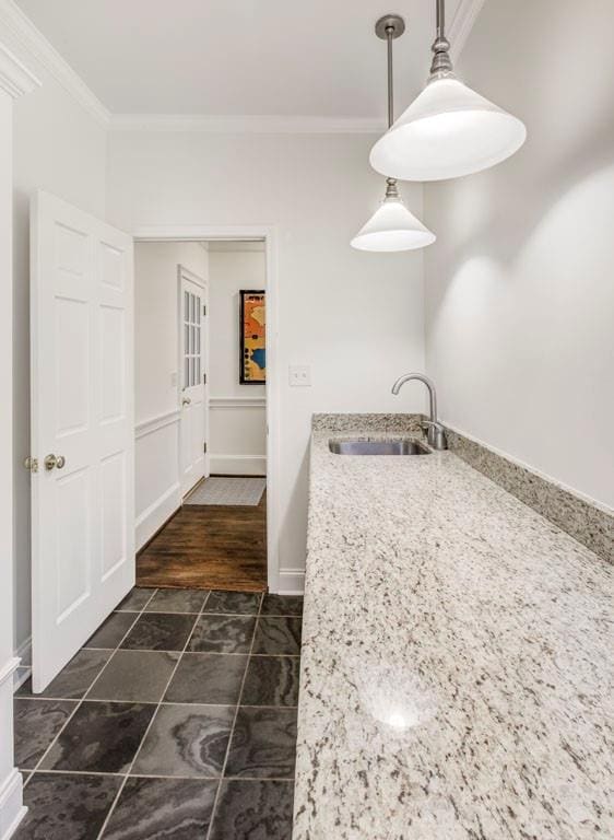 kitchen with light stone counters, hanging light fixtures, crown molding, and sink