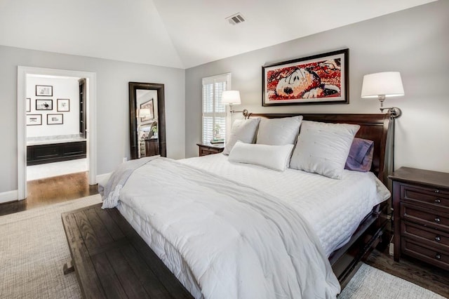 bedroom with connected bathroom, wood-type flooring, and vaulted ceiling