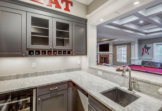 kitchen with sink, coffered ceiling, dark brown cabinetry, light stone countertops, and beverage cooler